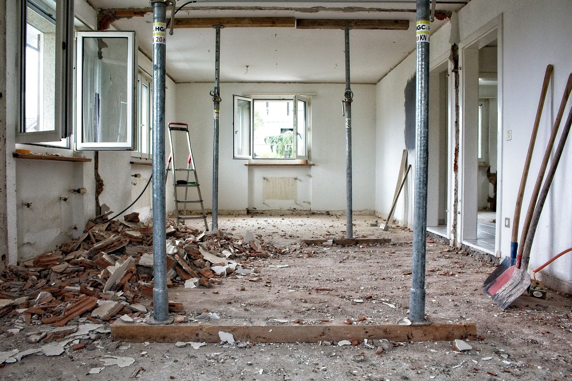A room under renovation with metal support poles, debris, and tools on the floor